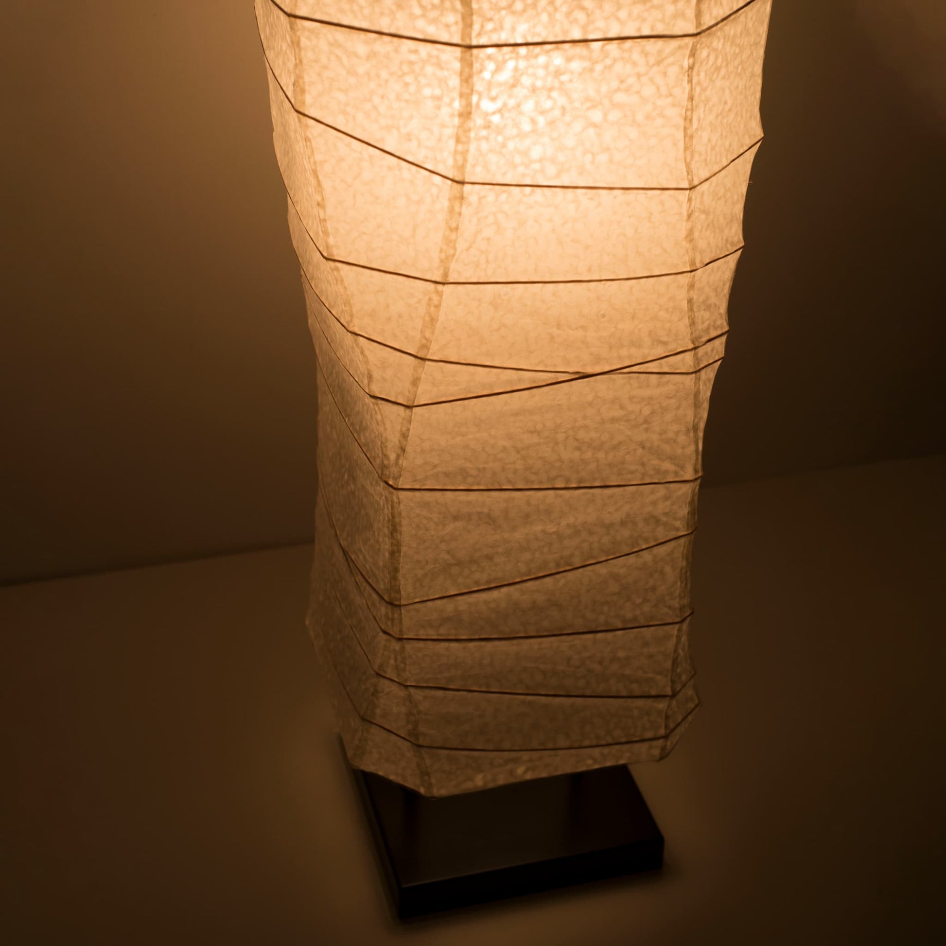 A close-up view of the lower part of a Japanese washi paper lamp, shot from above, showcasing its elegant curves and warm light