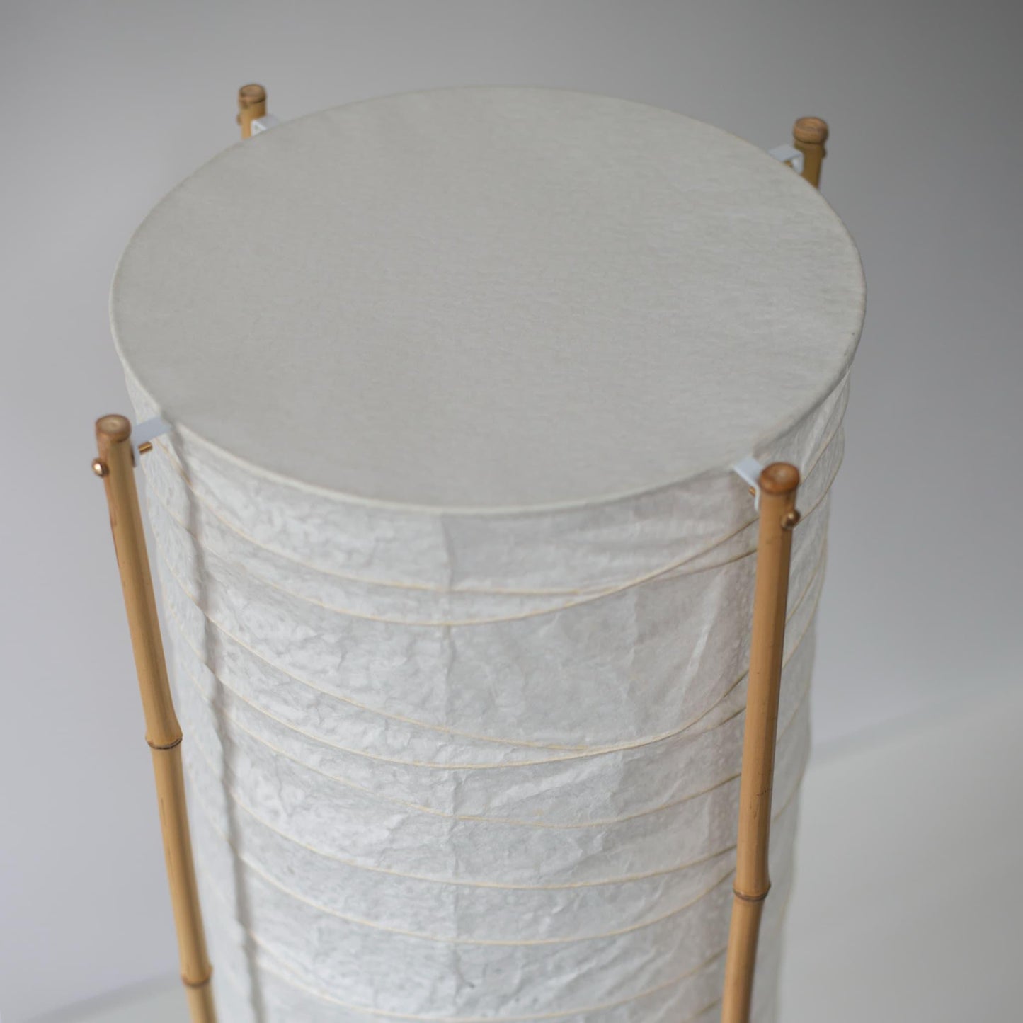 Close-up of the top section of a cylindrical Japanese lamp with bamboo frame and washi paper, white background
