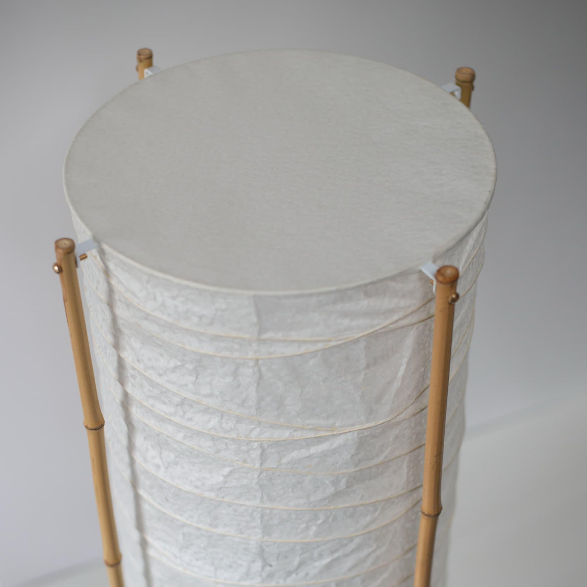 Close-up of the top section of a cylindrical Japanese lamp with bamboo frame and washi paper, white background