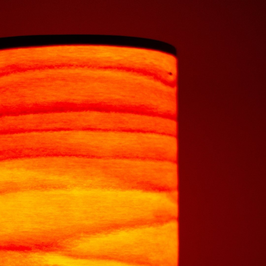 Close-up of cylindrical Japanese table lamp casting flame-like light through thin wood slats.