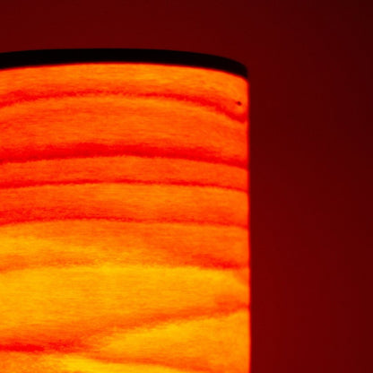 Close-up of cylindrical Japanese table lamp casting flame-like light through thin wood slats.