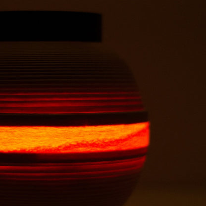 Close-up of Japanese living room lamp with warm light band glowing through beech wood slats.