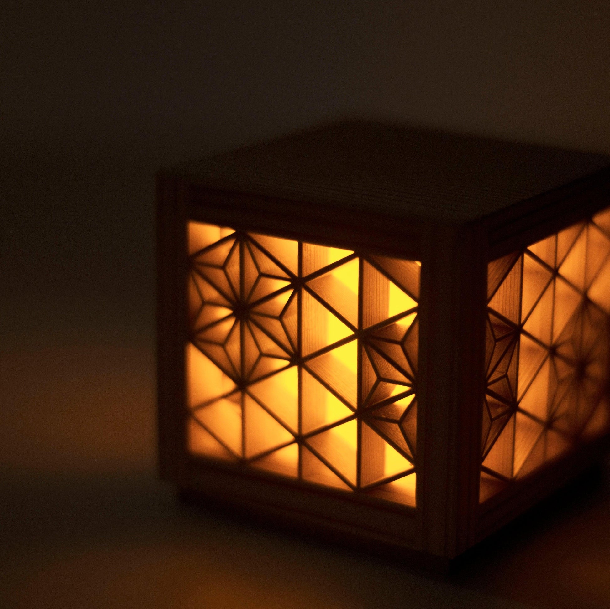 A close-up of an intricate kumiko light fixture, showcasing the delicate wooden latticework and warm LED glow.