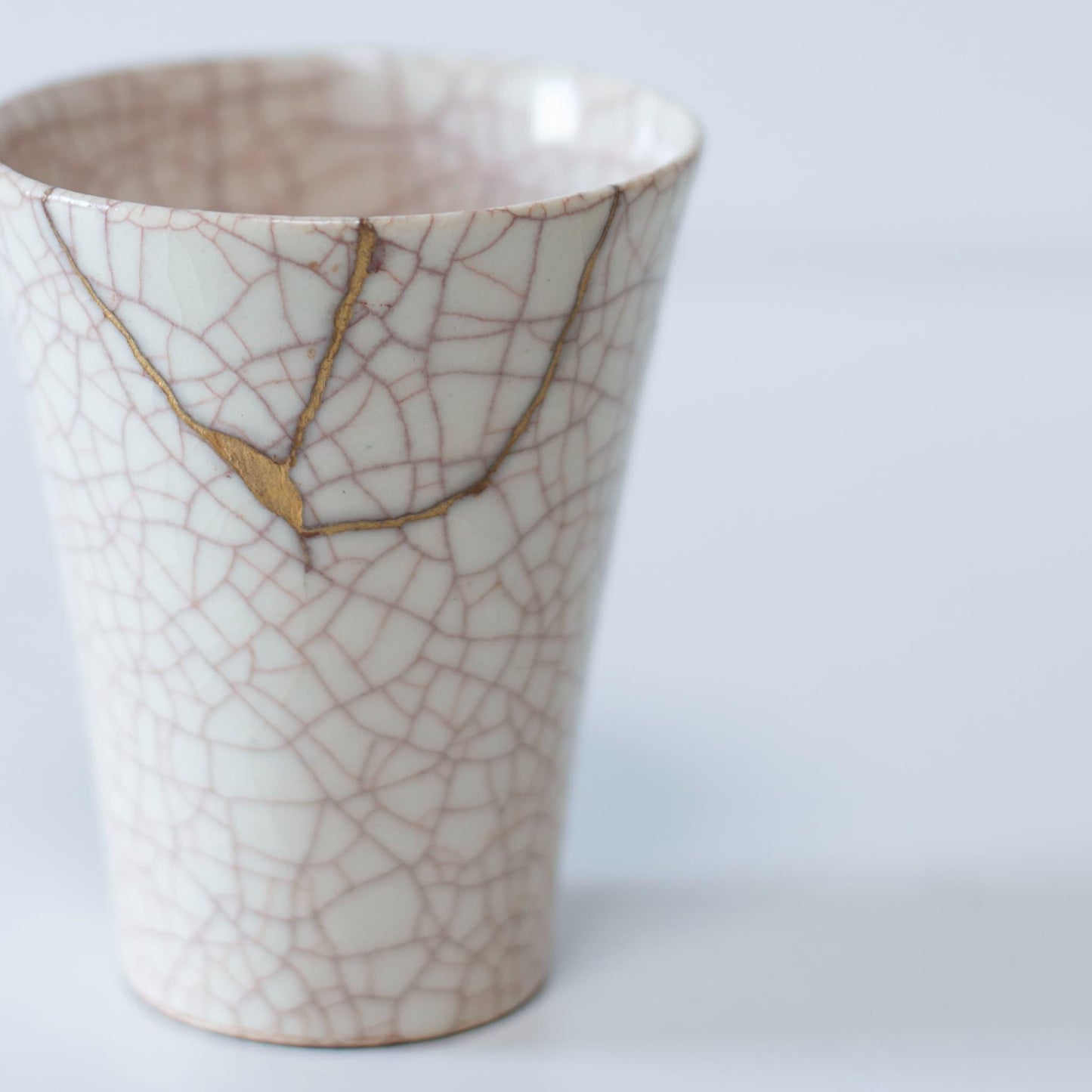 White cup repaired with Kintsugi, a traditional Japanese technique, presented in a paulownia wood box with the inscription "Kintsugi".