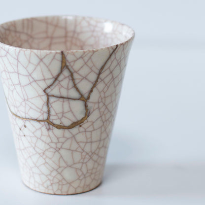 White cup repaired with Kintsugi, a traditional Japanese technique, presented in a paulownia wood box with the inscription "Kintsugi".