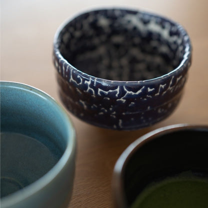 A grouping of three Japanese matcha bowls, with the "Midnight Blue Kairagi" bowl centered, showcasing its unique textured glaze alongside a light blue and a dark brown chawan.
