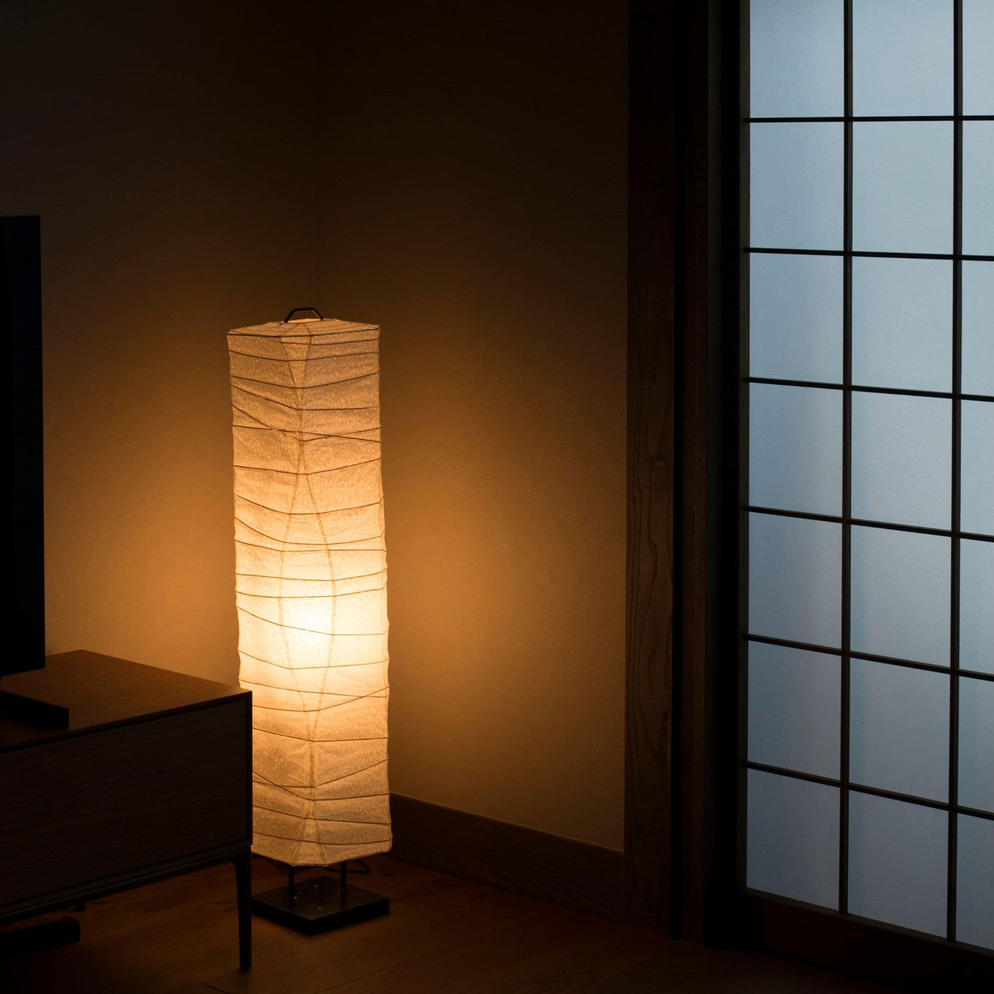 A glowing Japanese paper floor lamp with curved lines, placed in the corner of a traditional Japanese room. 