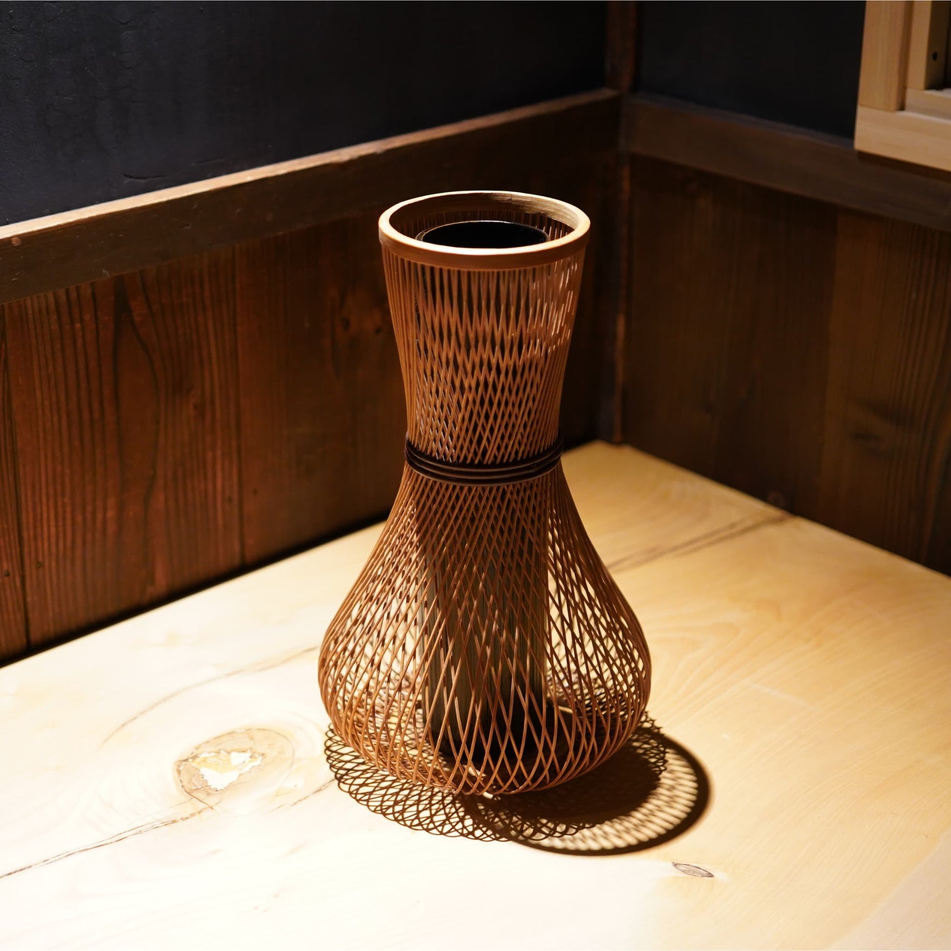 A cylindrical Japanese ikebana vase with a rounded, bulbous base, made from bamboo with beautifully intricate, interwoven strips.