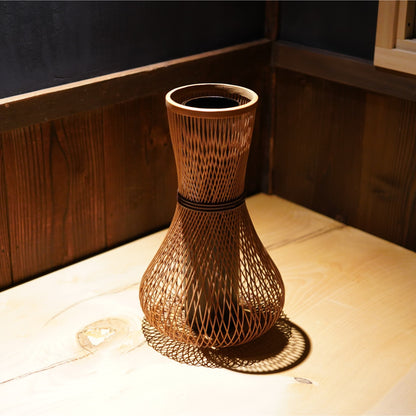 A cylindrical Japanese ikebana vase with a rounded, bulbous base, made from bamboo with beautifully intricate, interwoven strips.