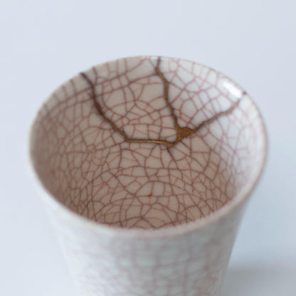 A close-up of the delicate kintsugi repair on the interior of a white ceramic cup, showcasing the Japanese aesthetic of wabi-sabi.