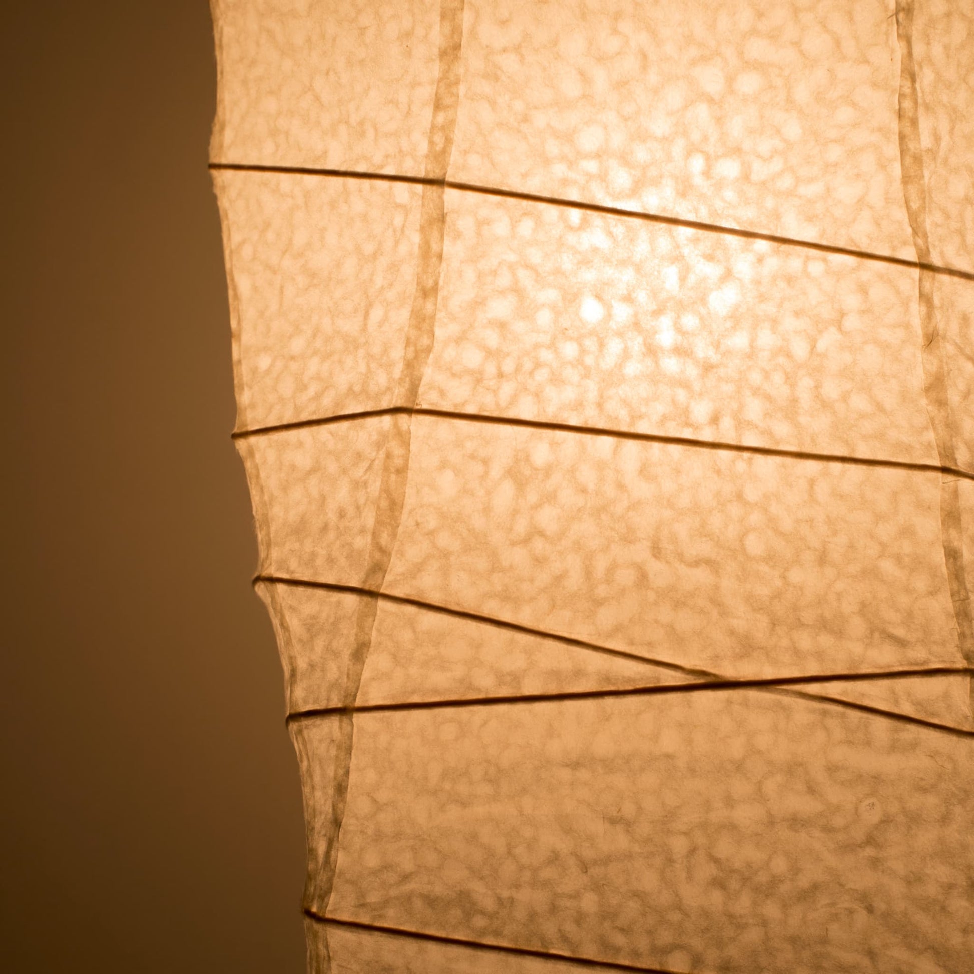 A close-up side view of a Japanese washi paper lamp, with warm light illuminating the detailed texture of the washi paper
