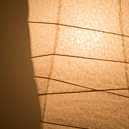 A close-up side view of a Japanese washi paper lamp, with warm light illuminating the detailed texture of the washi paper