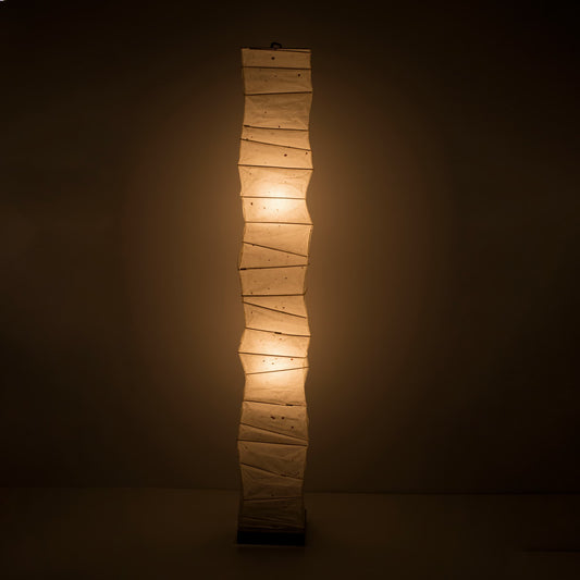 Full front view of a tall, randomly curved Japanese washi paper lamp emitting a warm glow on a dark brown background
