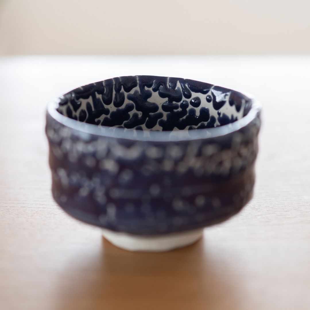 A Japanese Shino Ware matcha chawan "Midnight Blue Kairagi" displayed on a wooden surface, emphasizing the bowl's form, the rich dark blue color, and the textured Kairagi glaze.