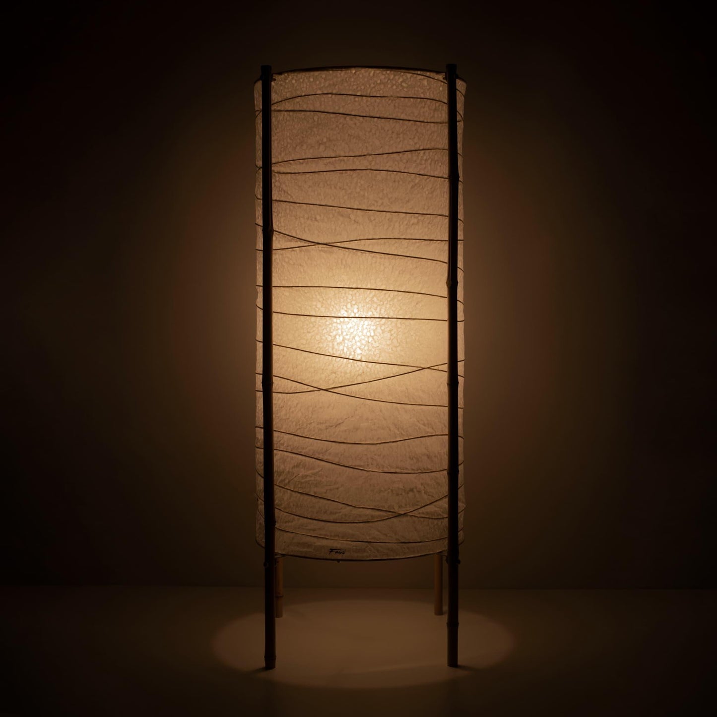 Full view of a cylindrical Japanese lamp with washi paper shade and bamboo frame, warm glow on brown background