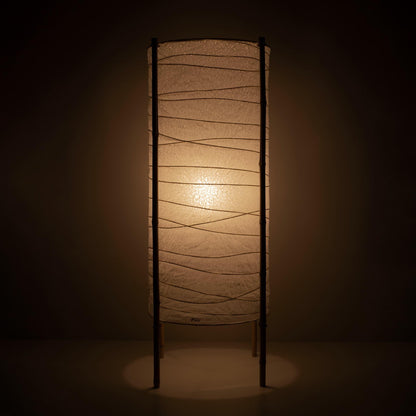 Full view of a cylindrical Japanese lamp with washi paper shade and bamboo frame, warm glow on brown background