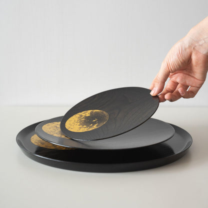 A close-up of a Japanese lacquerware plate featuring a moon design in gold leaf.