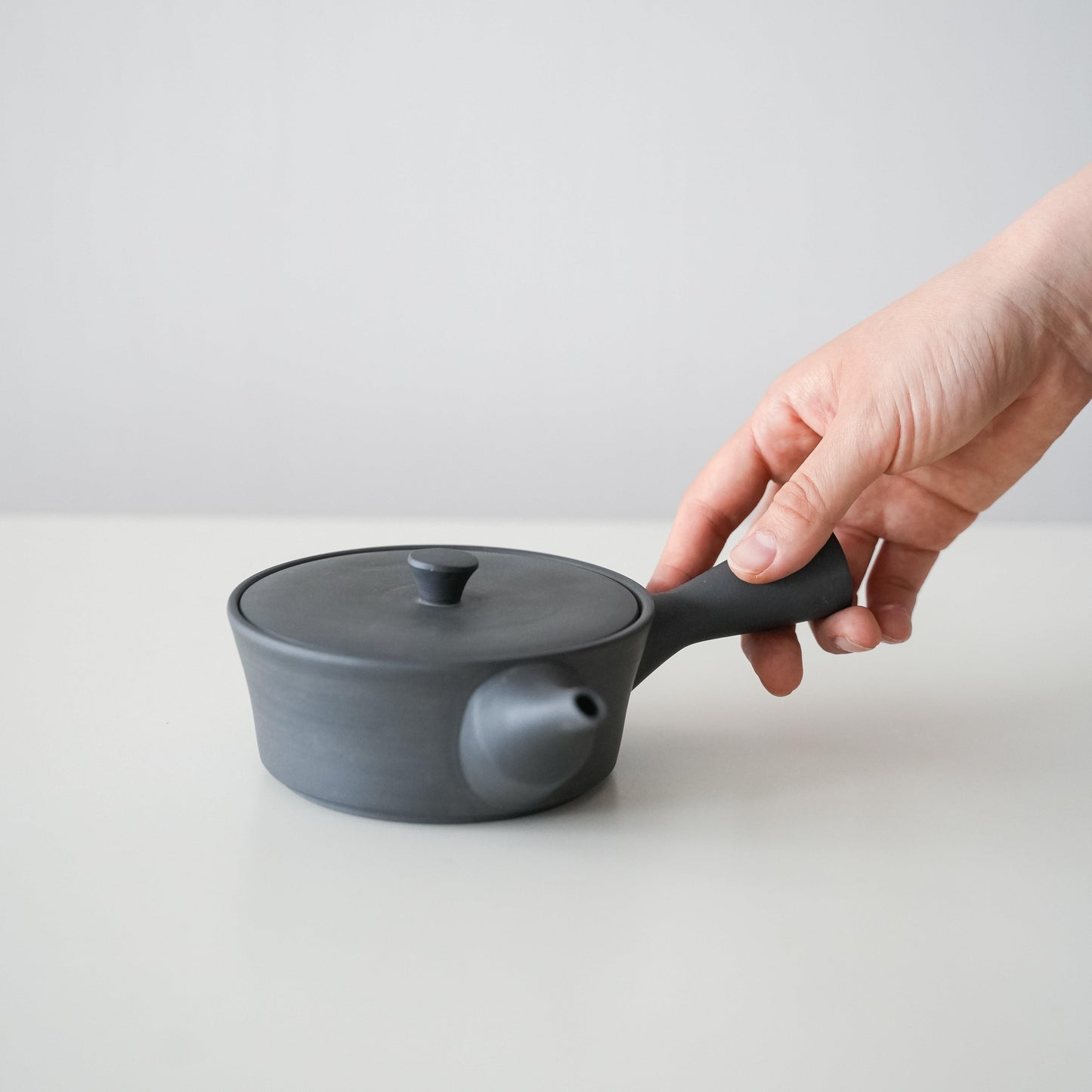 A hand holding a simple and beautiful black Banko ware teapot.