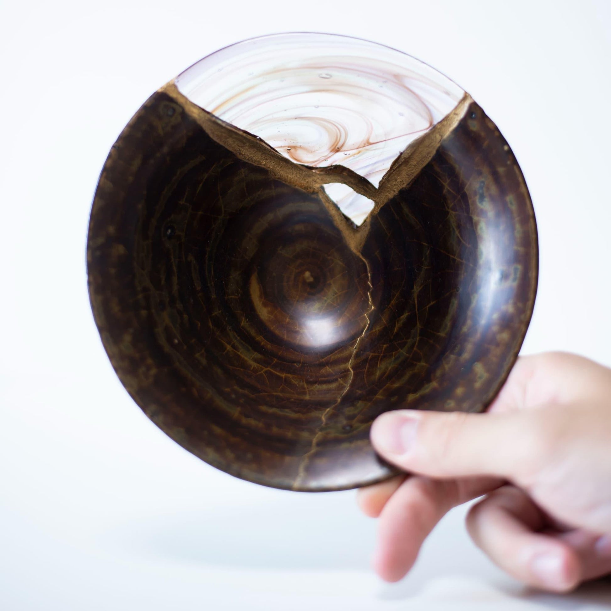 A hand holding a Kintsugi bowl, showcasing the weight and balance of the piece.