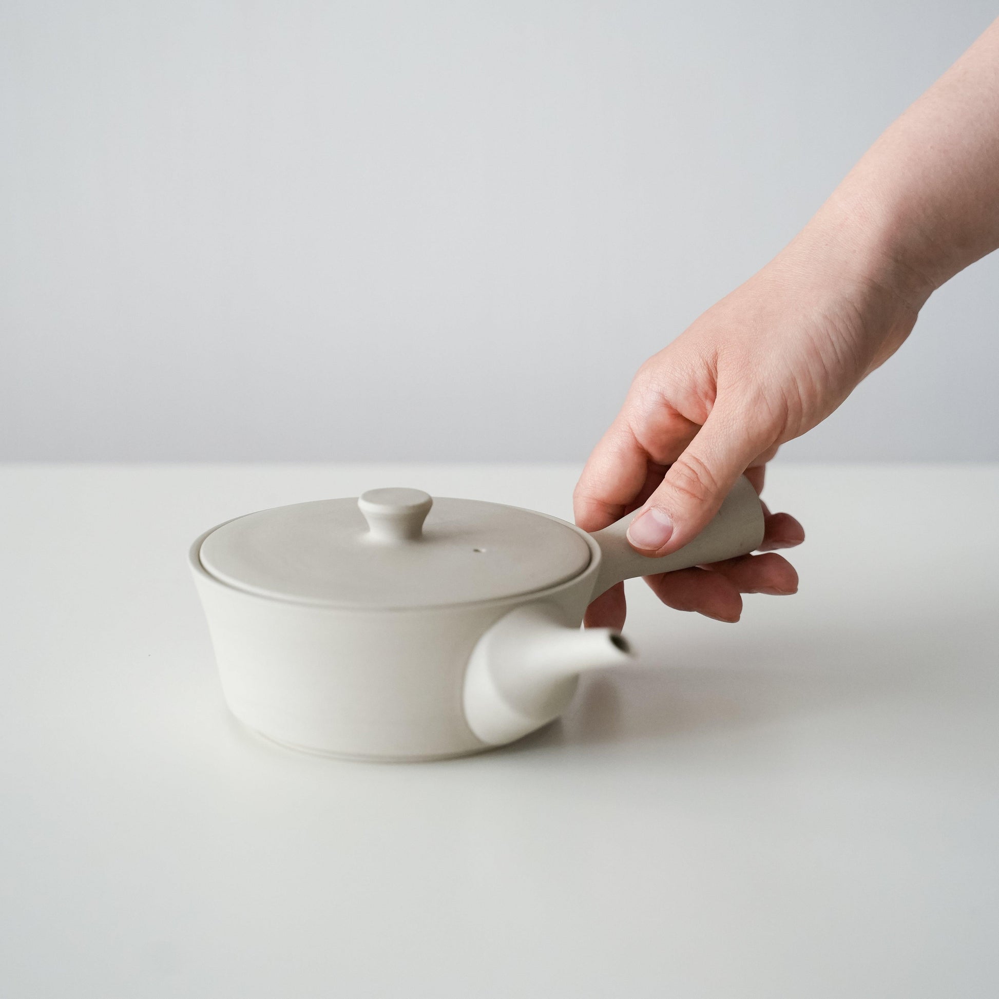 A hand holding a simple and beautiful white Banko ware teapot.