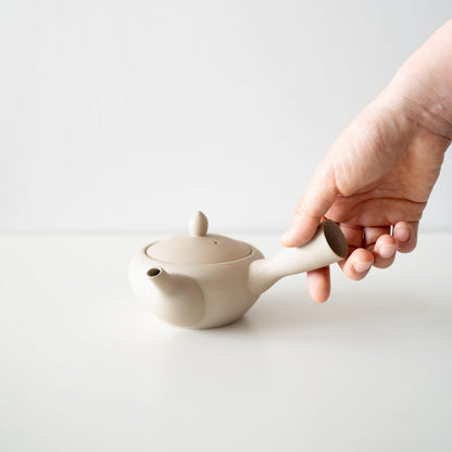 A hand holding a simple and soft-shaped white Banko ware teapot.