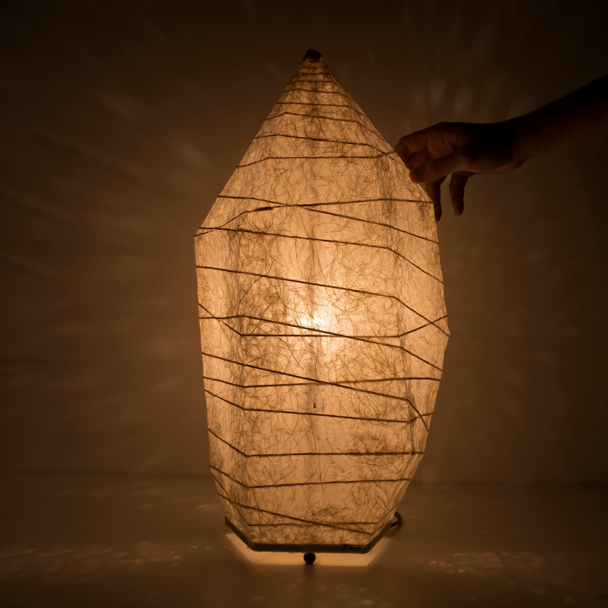 A hand touches the top of a Japanese paper floor lamp with ice stone design and warm glow, made from traditional washi paper