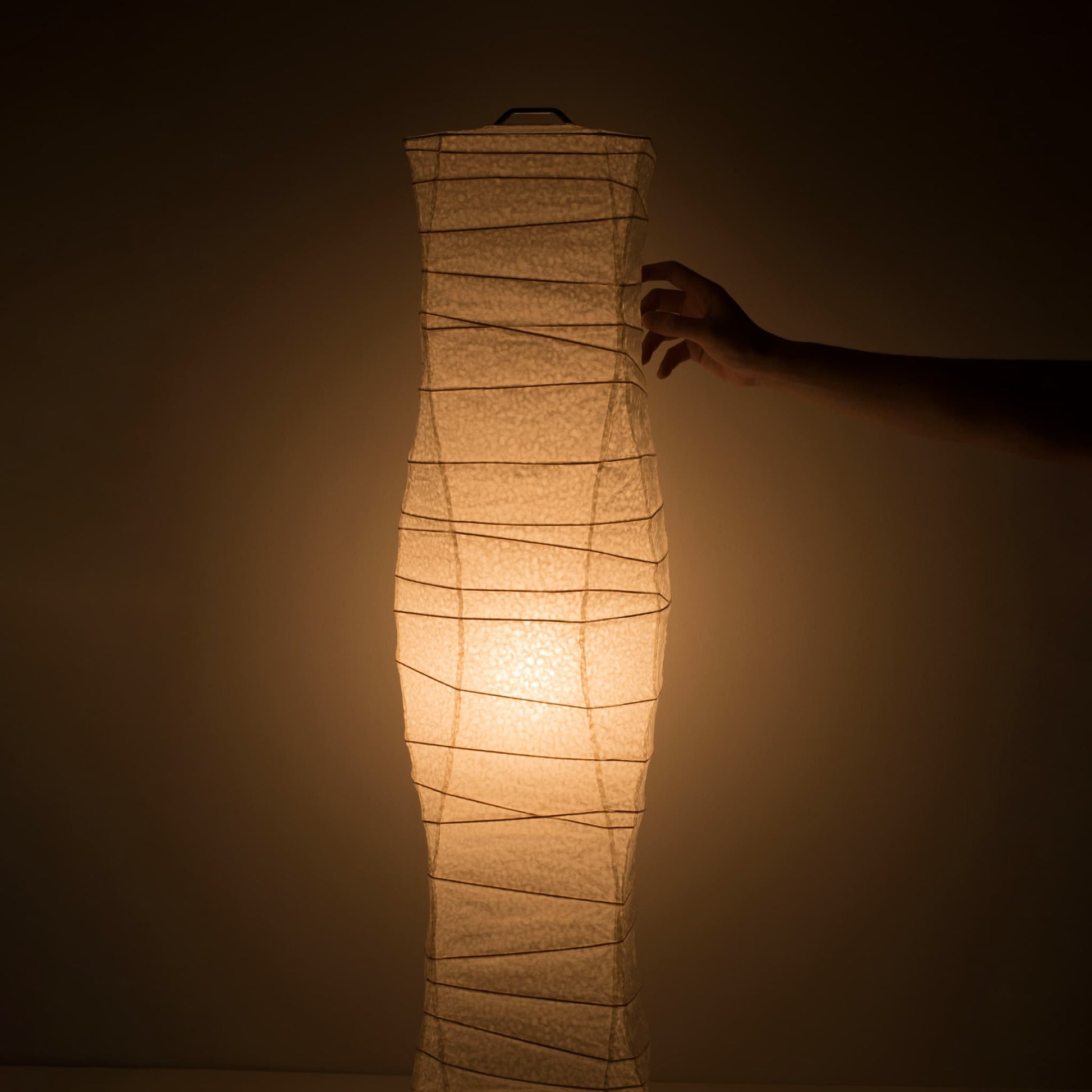 A hand gently touches the side of a Japanese washi paper lamp with flowing curves, emitting a soft, warm glow