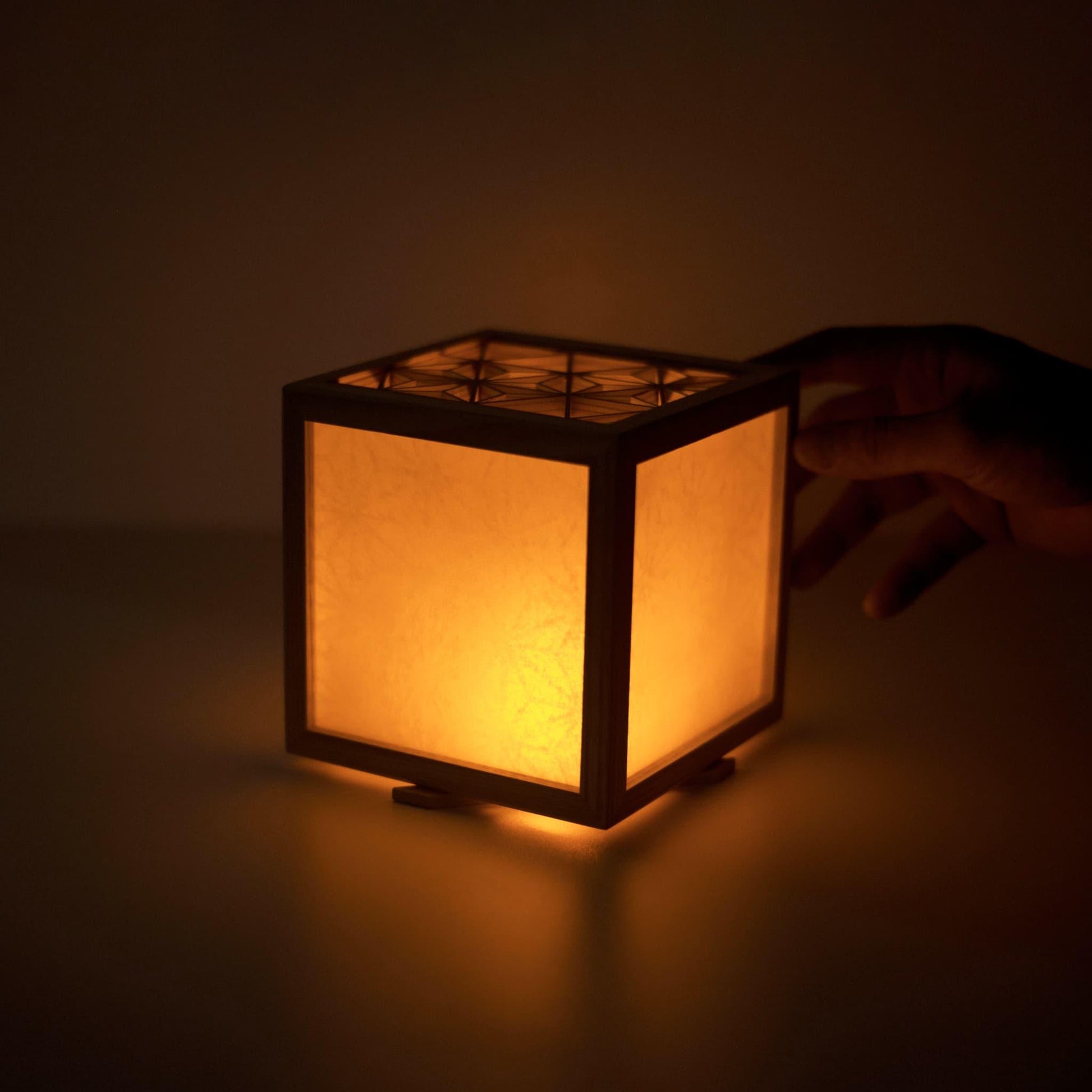 A hand gently touching a medium-sized kumiko lighting cover, highlighting the craftsmanship and warmth of the piece.