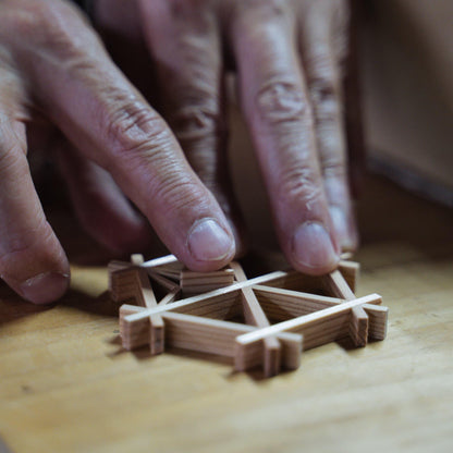 Hands of a craftsman creating traditional Japanese kumiko, a technique of assembling small wooden pieces into geometric patterns.