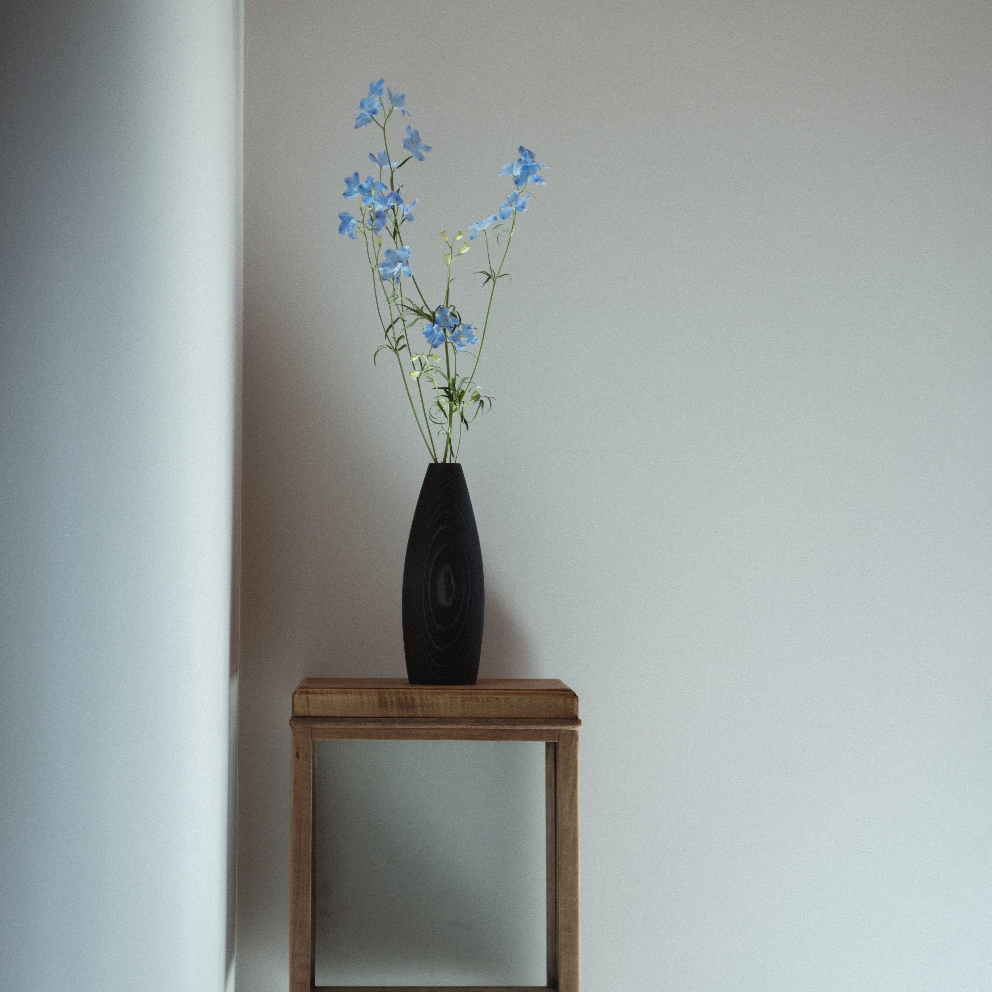 A simple indigo-dyed vase made of natural Japanese cedar, placed in a minimalist Japandi-style living room.