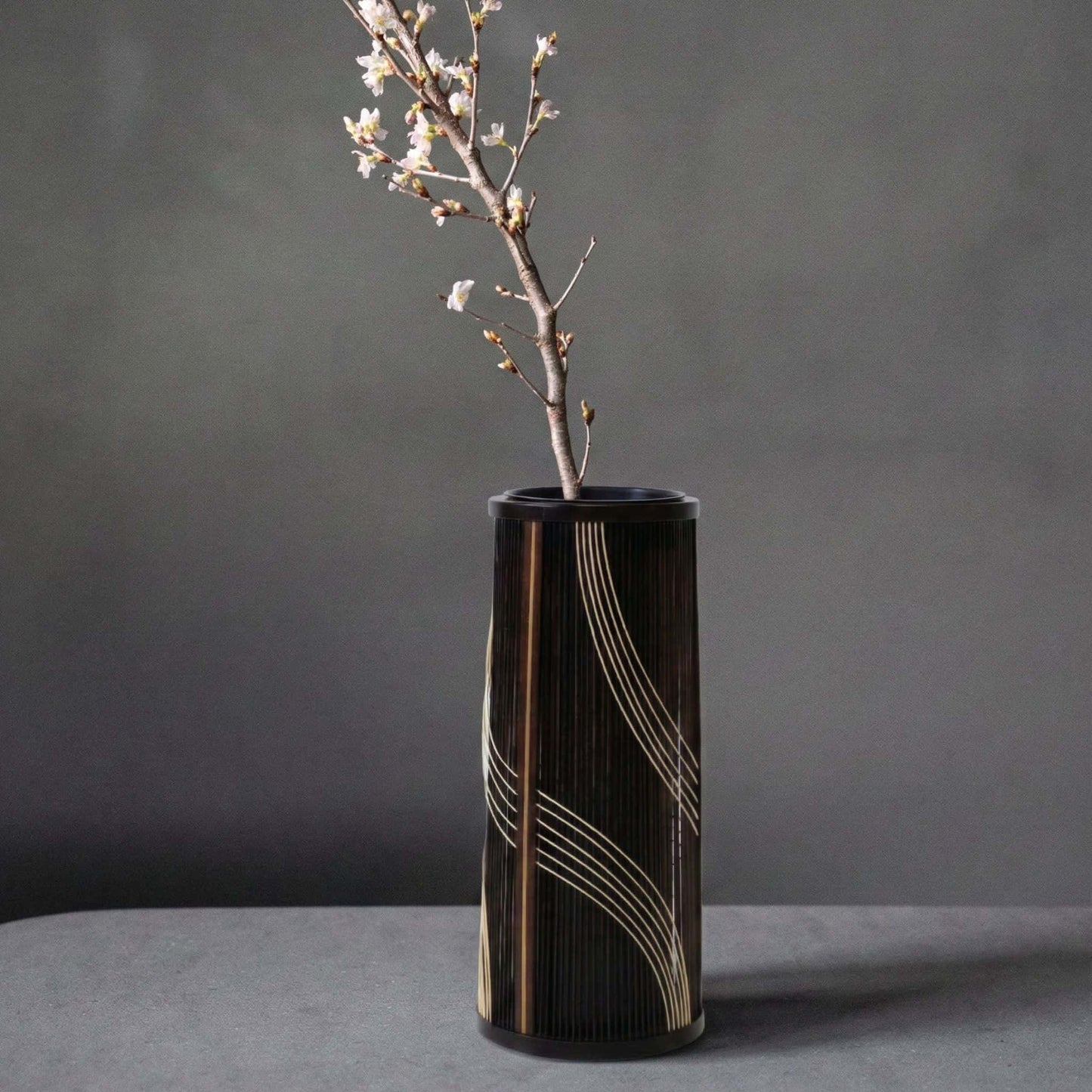 Japanese bamboo vase titled "Flowing Water" displayed on a gray hotel table.