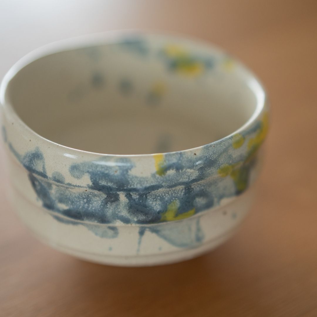 High-angle view of the "Splash" matcha chawan bowl, featuring vibrant blue and yellow glaze spots on white Shino clay, inspired by the cooling tradition of Uchimizu in Japanese summer.