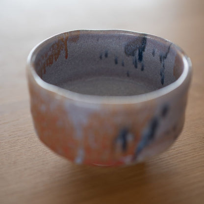 Overhead, slightly angled view showing the interior and exterior of the Navy and Red Splash Japanese matcha bowl. The abstract, deep-colored glaze drips and the subtle Kinyo purple interior are visible.