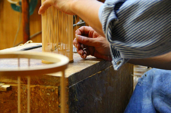 An artisan crafting interior items using finely processed bamboo strips.