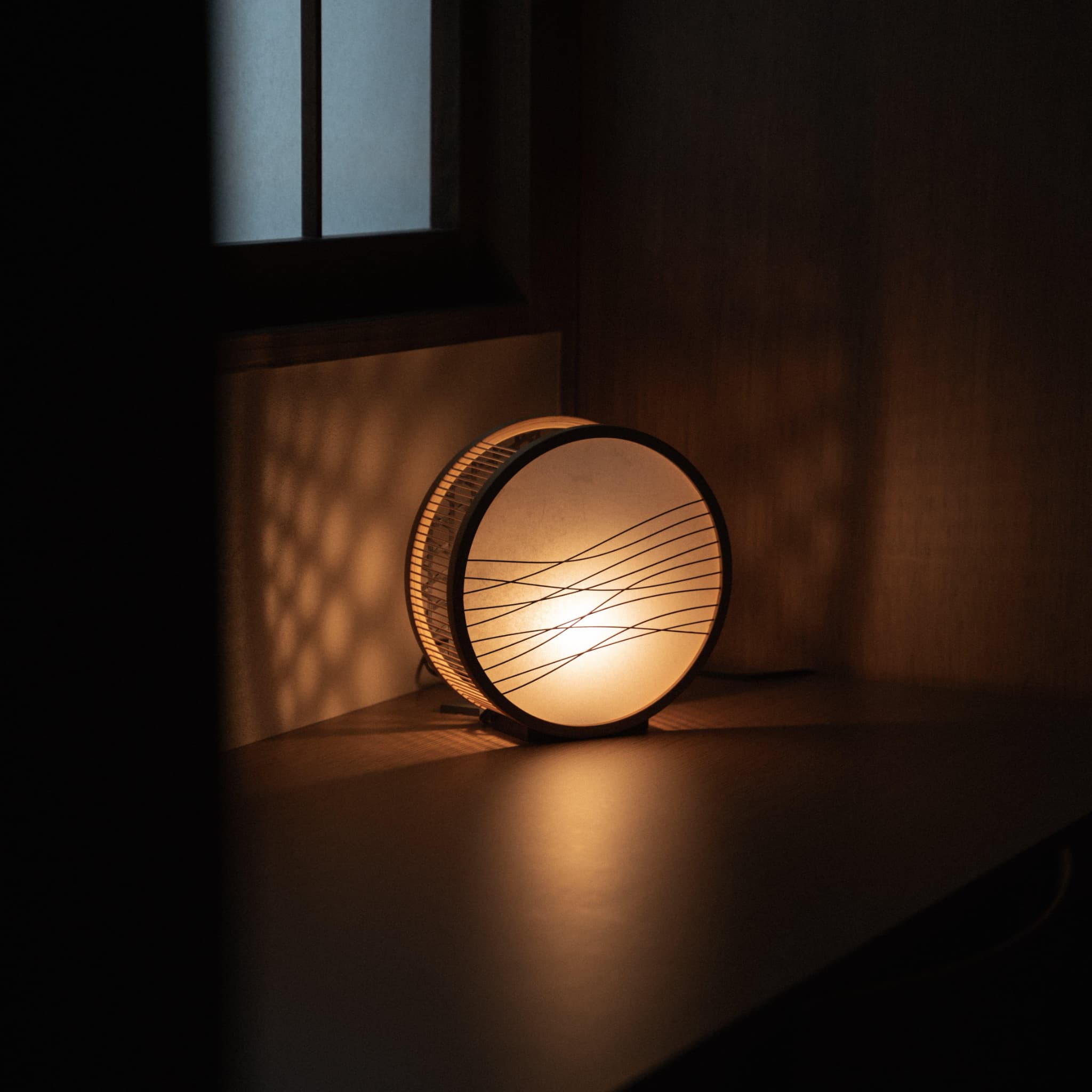 Traditional Japanese bamboo lamp handcrafted in Shizuoka with 800-year-old techniques, casting an ethereal glow on a bedroom table.