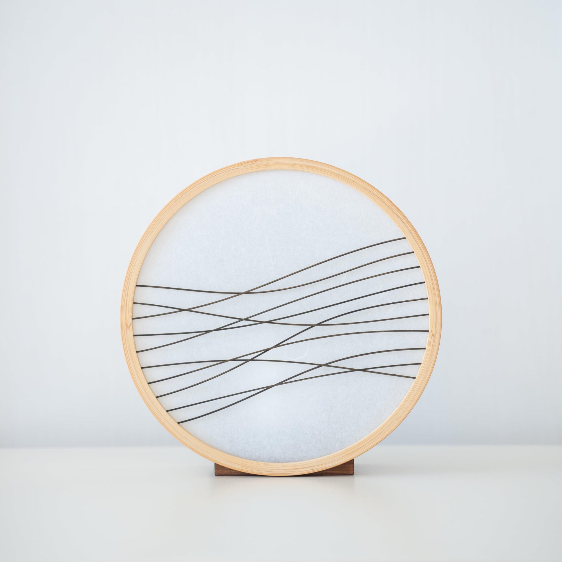 Traditional Japanese bamboo lamp handcrafted in Shizuoka with 800-year-old techniques. Circular wooden frame with washi paper shade featuring delicate bamboo accents. Simple yet elegant design casts a soft, warm glow.