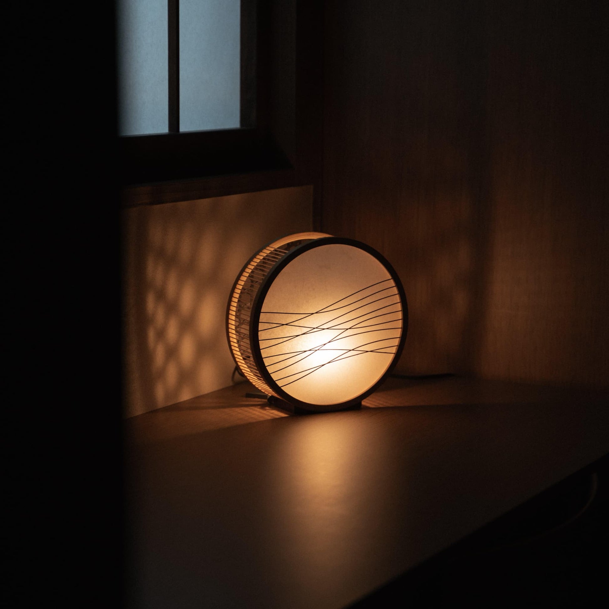 Traditional Japanese bamboo lamp handcrafted in Shizuoka with 800-year-old techniques, casting an ethereal glow on a bedroom table.
