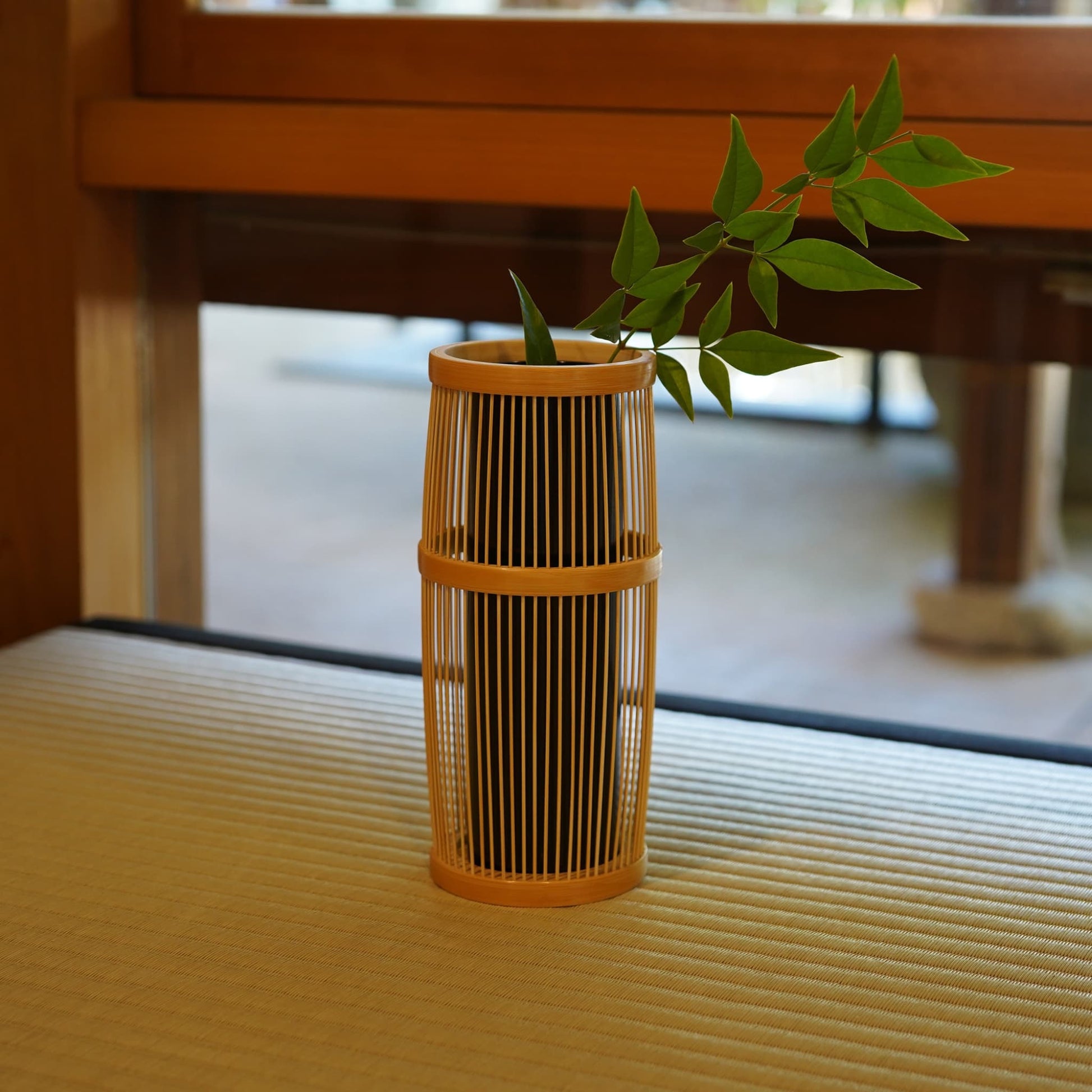 A Japanese ikebana vase holding green plants, placed on a tatami mat in a traditional Japanese room.