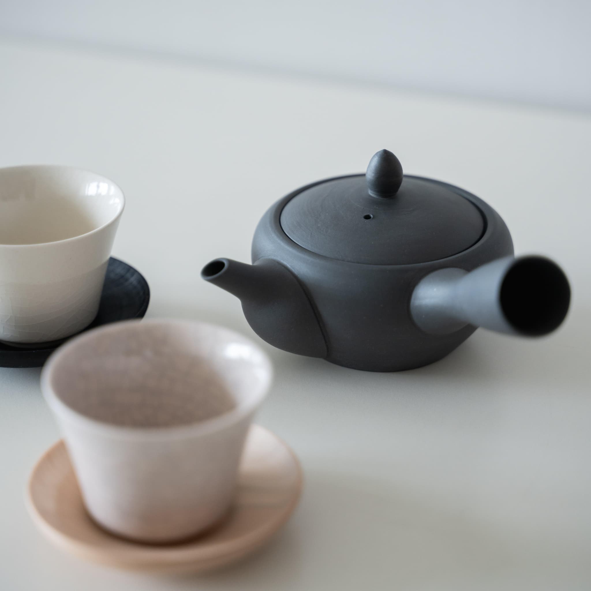 Traditional Japanese Banko-yaki black teapot and two white teacups with crazing, showcasing the beauty of wabi-sabi aesthetics.