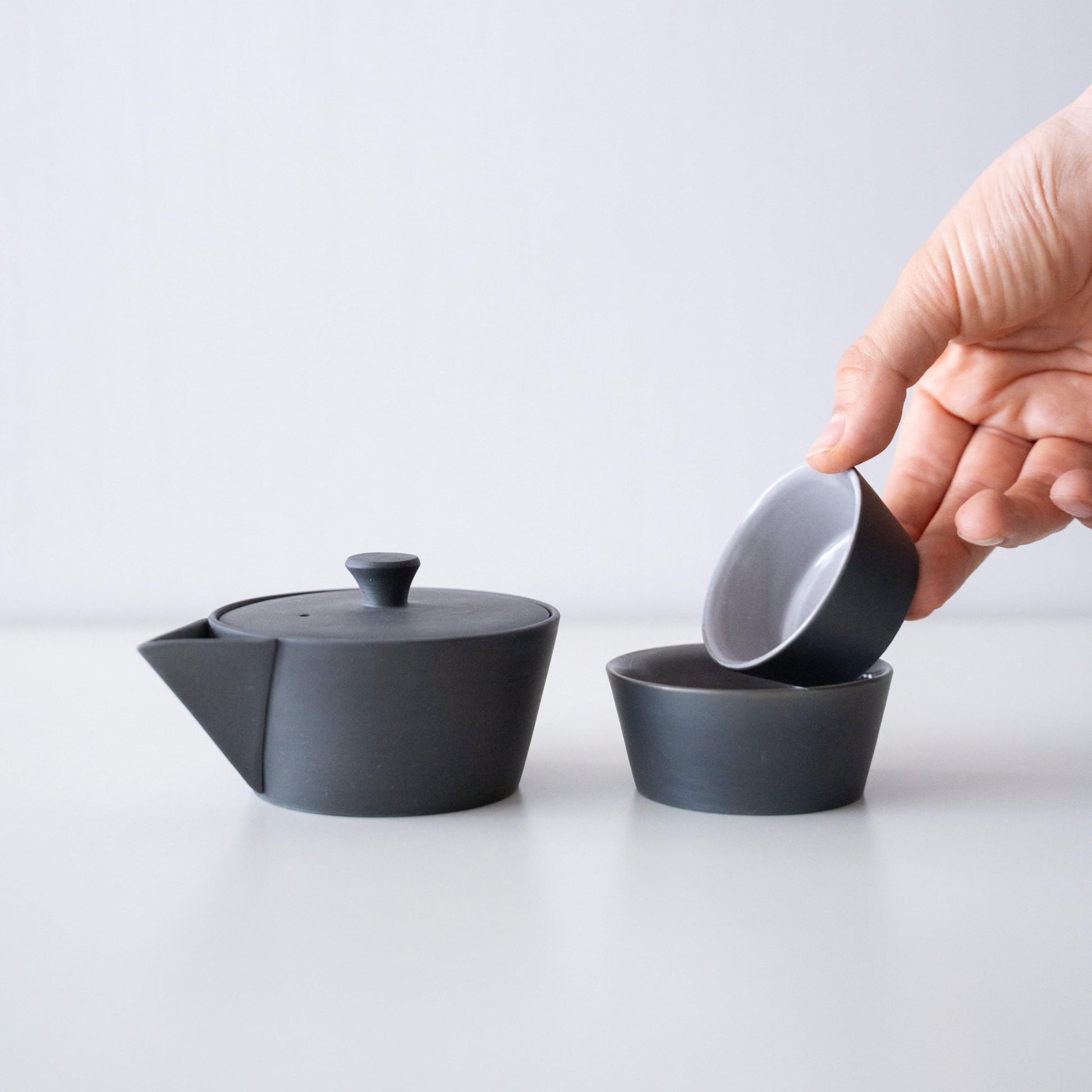 Hand holding a Japanese Banko-yaki black teapot and two cups nesting set, with a history of several hundred years.