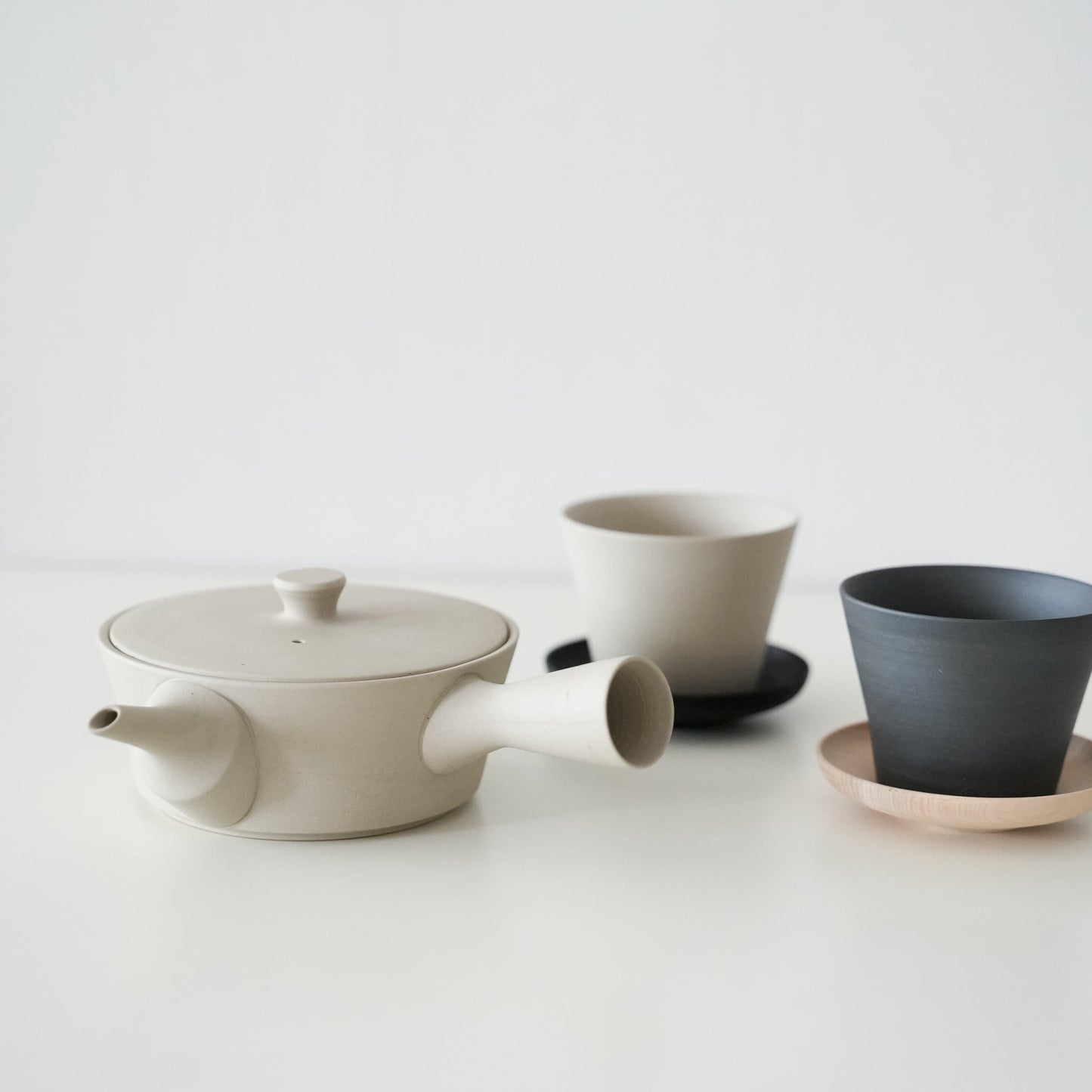 A simple and beautiful white Banko ware teapot with a black and white Banko ware teacup on a wooden coaster.