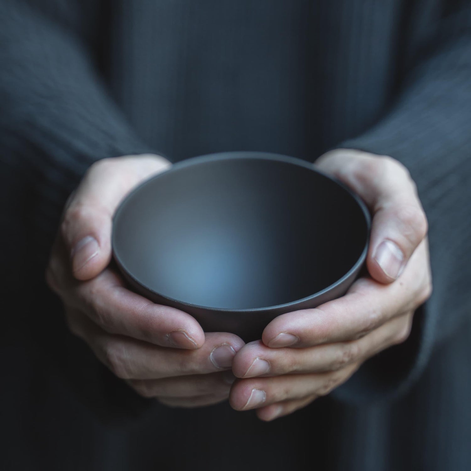 Holding a black Japanese bowl with both hands as if cradling it.