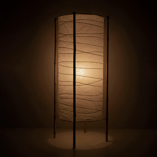 Full view of a Japanese lamp with cylindrical washi paper shade and bamboo frame, warm glow on brown background