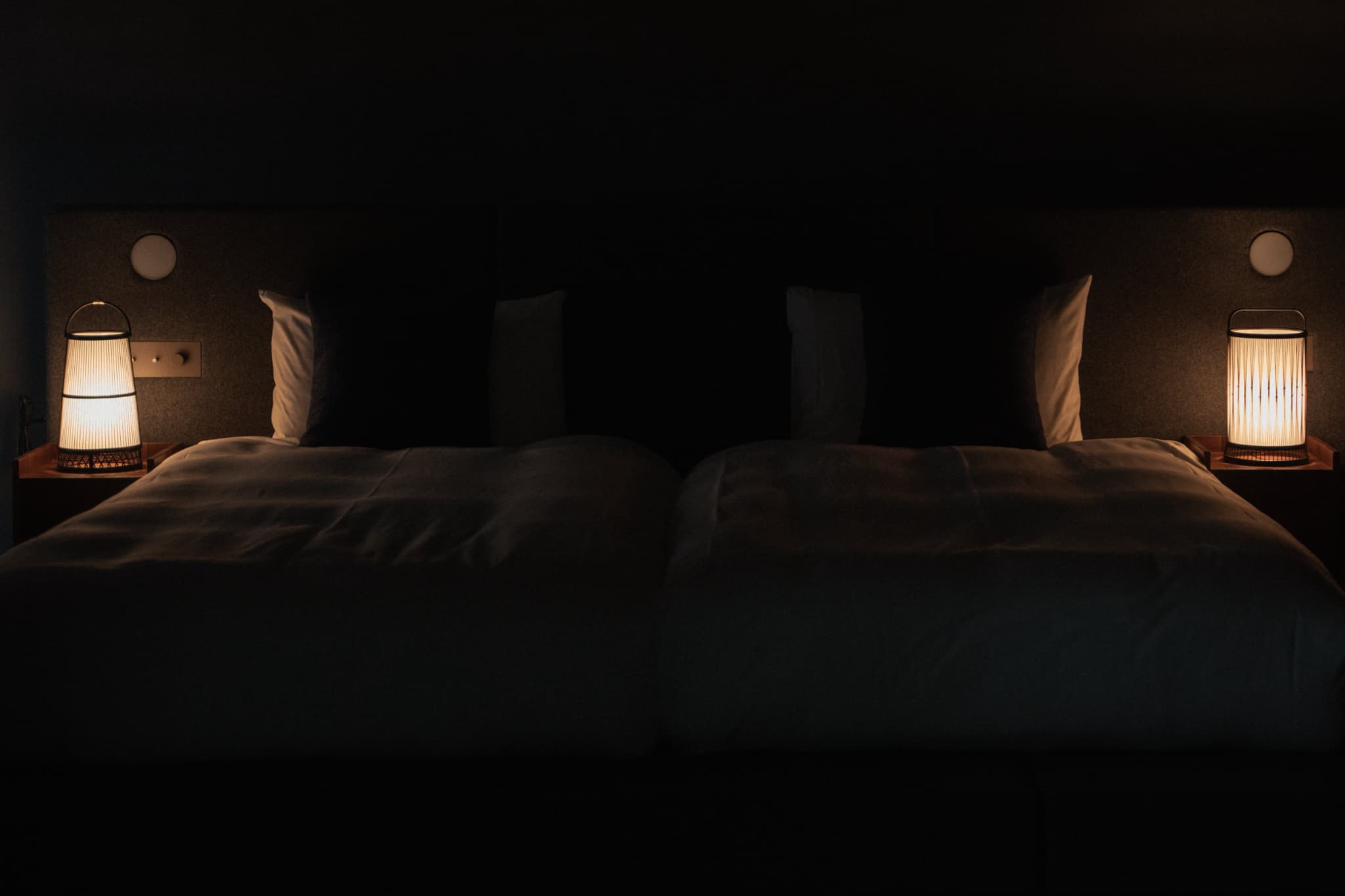 Two traditional Japanese bamboo floor lamps, handcrafted in Shizuoka, illuminate a Japandi-style bedroom.