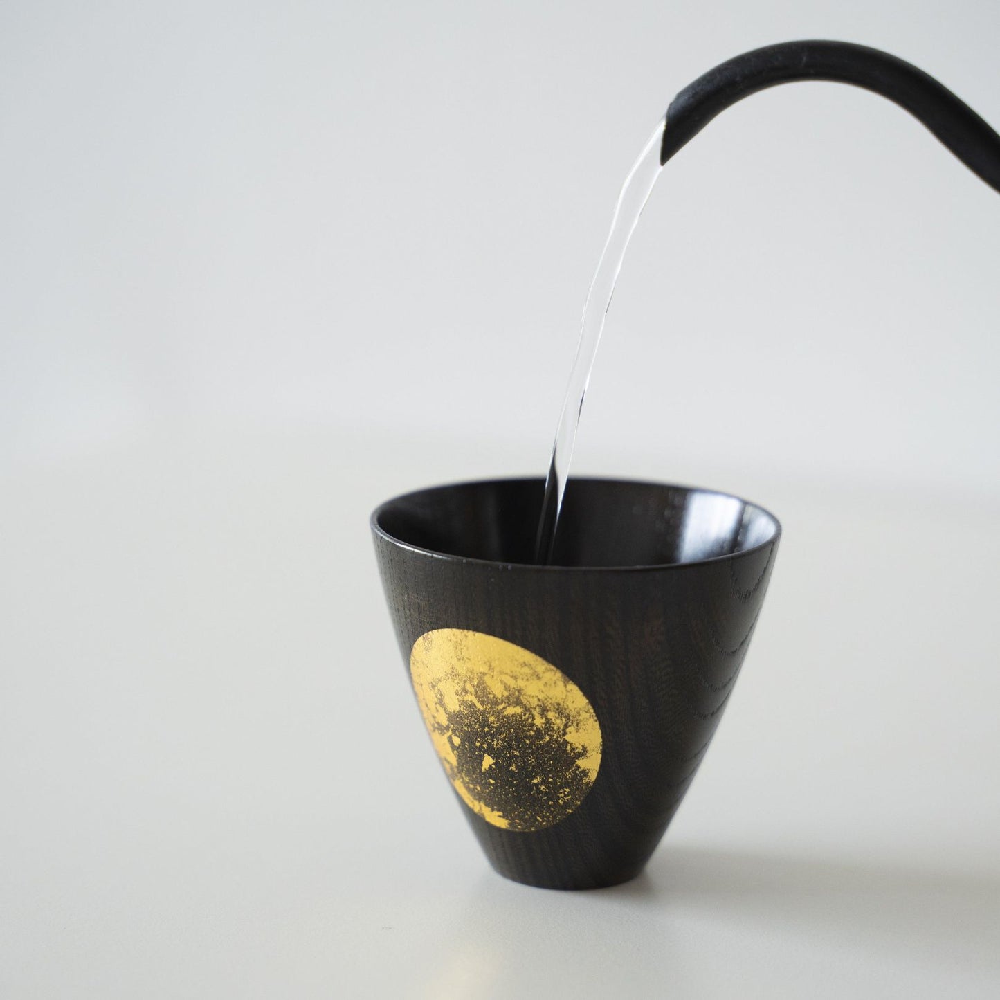 Water is being poured into a Japanese lacquerware sake cup.