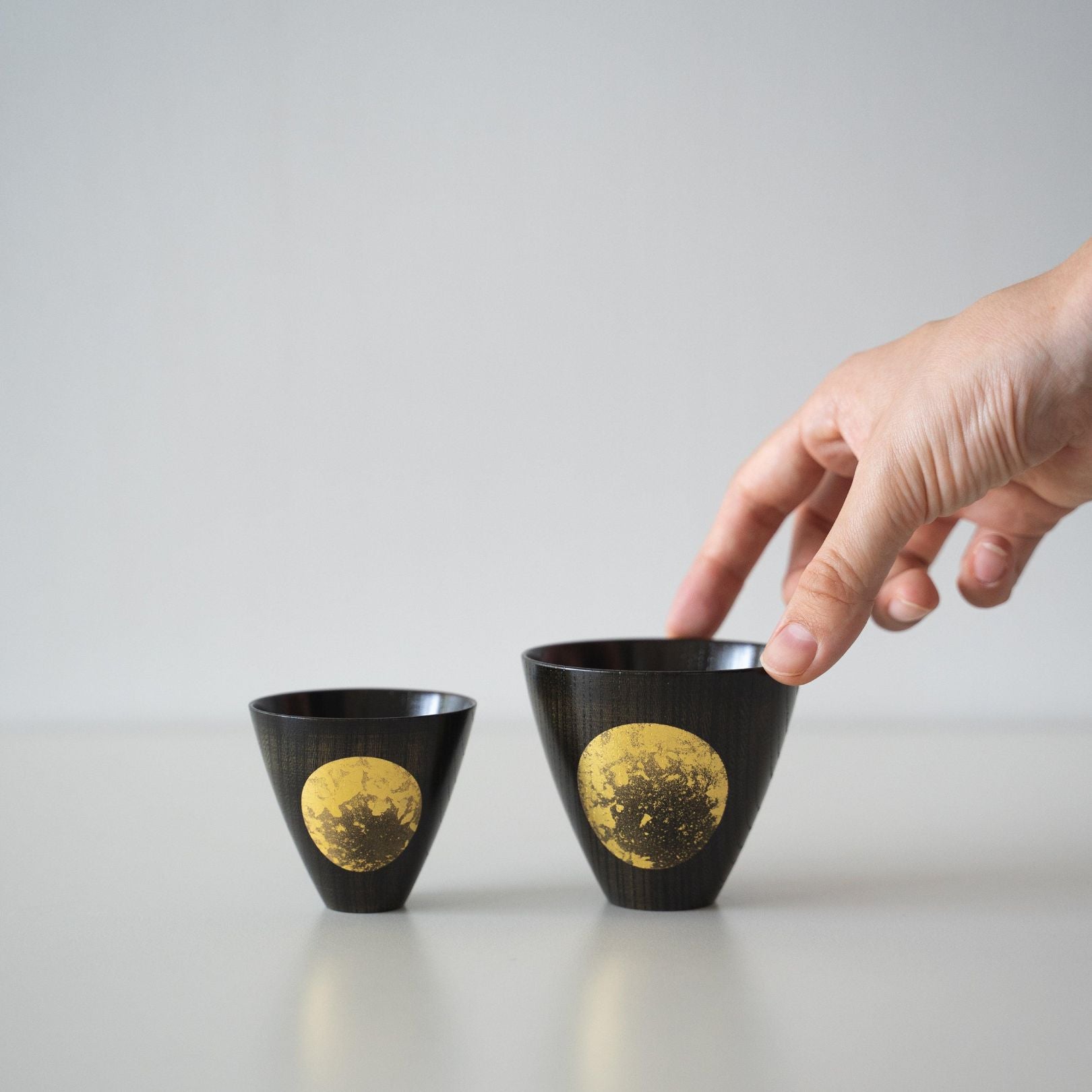 One of the two Japanese lacquerware sake cups placed side by side is being held in hand.