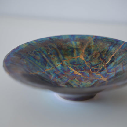 Iridescent bowl repaired with Kintsugi, a traditional Japanese technique that embraces the beauty of imperfection.