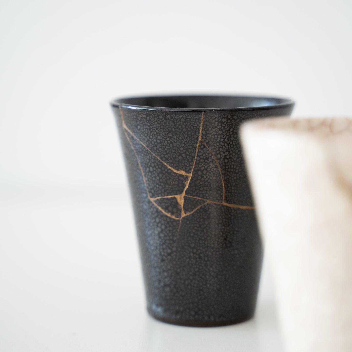 Two Japanese Kintsugi cups, one black and one white, repaired with gold lacquer using the traditional Kintsugi technique.