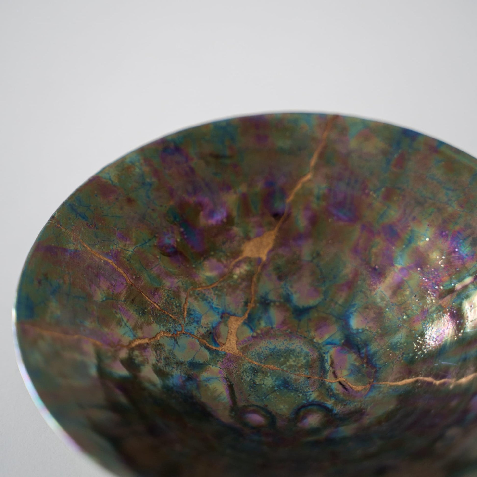 Close-up of a deep green sake cup repaired with Kintsugi, a traditional Japanese technique, showcasing the beautiful golden joinery.
