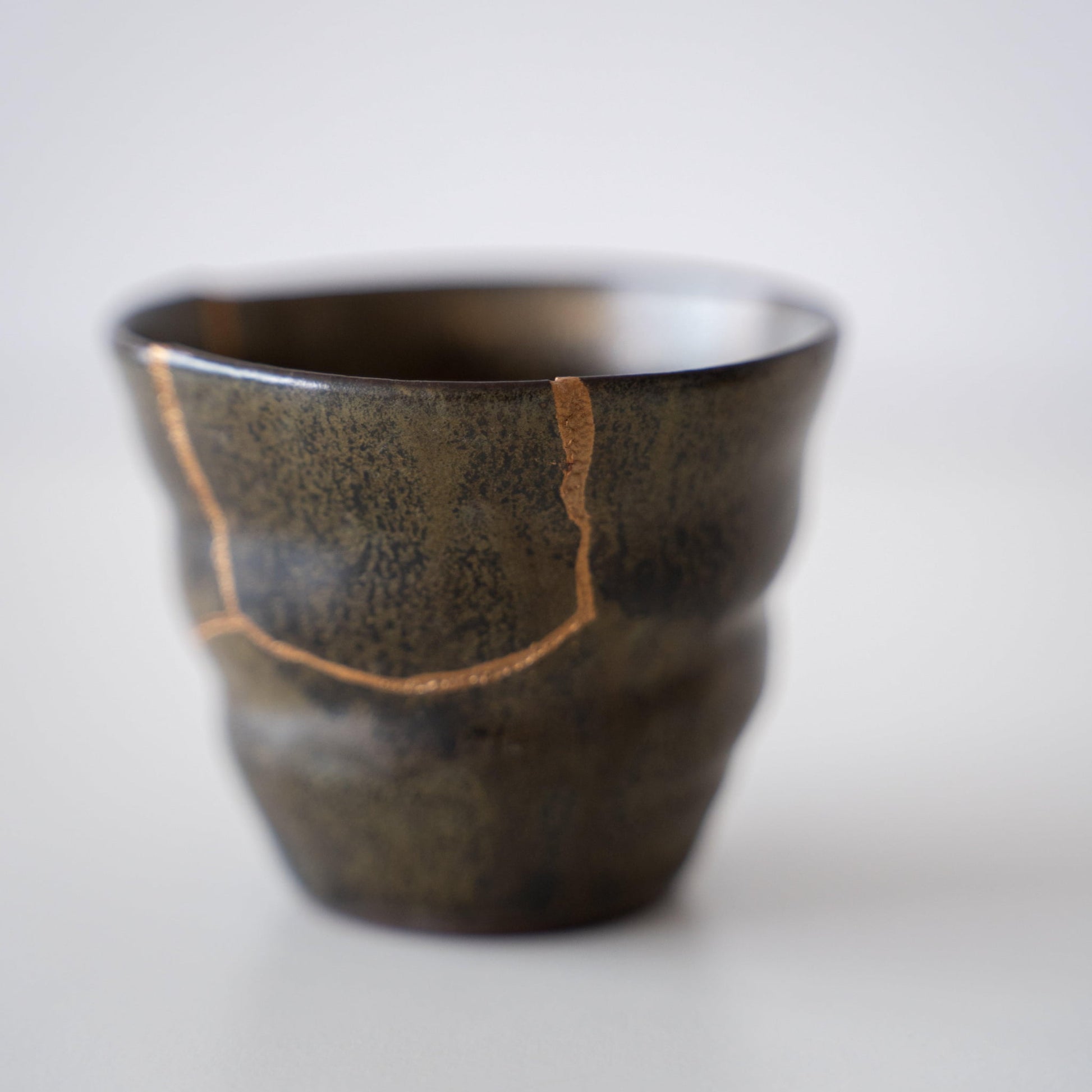 Close-up of a deep green sake cup repaired with Kintsugi, a traditional Japanese technique, showcasing the beautiful golden joinery.